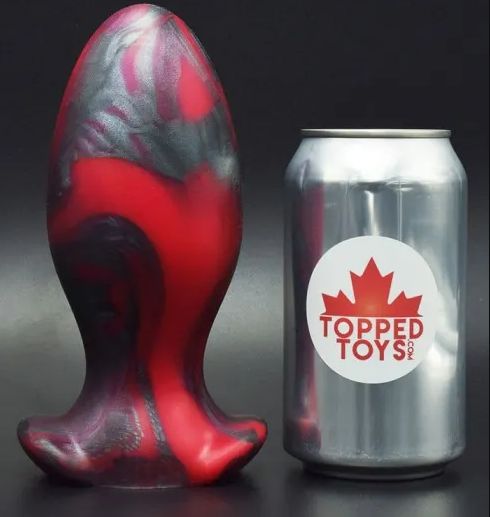 A substantial red and black colored butt plug, pictured beside a 12 oz. beverage can